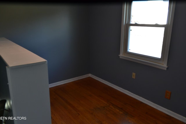 spare room with baseboards and dark wood-style flooring