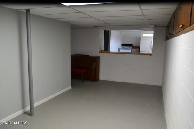 finished basement featuring a drop ceiling, concrete block wall, baseboards, and freestanding refrigerator