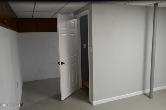 finished basement featuring a drop ceiling, concrete block wall, and baseboards