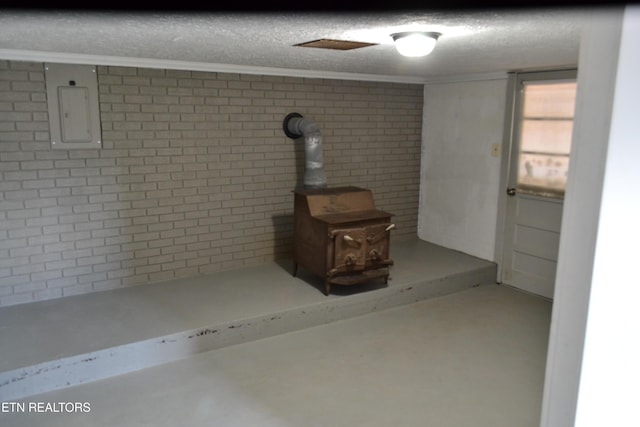 basement featuring crown molding, electric panel, brick wall, and a textured ceiling