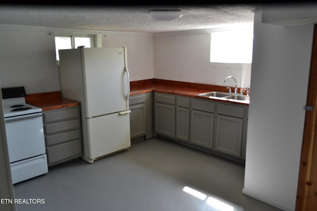 kitchen featuring a sink, a textured ceiling, white appliances, concrete floors, and concrete block wall