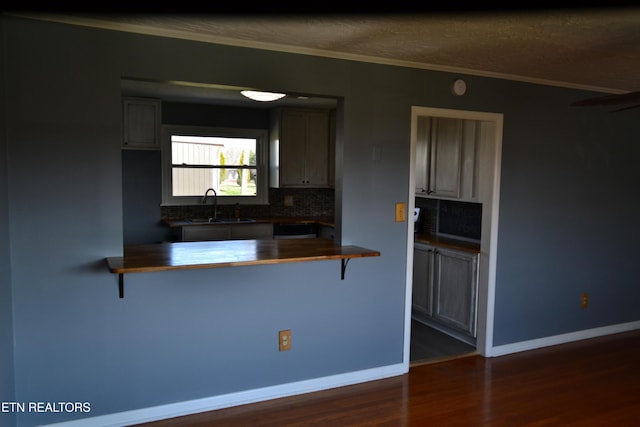 kitchen featuring a kitchen bar, butcher block countertops, a sink, dark wood-style floors, and decorative backsplash