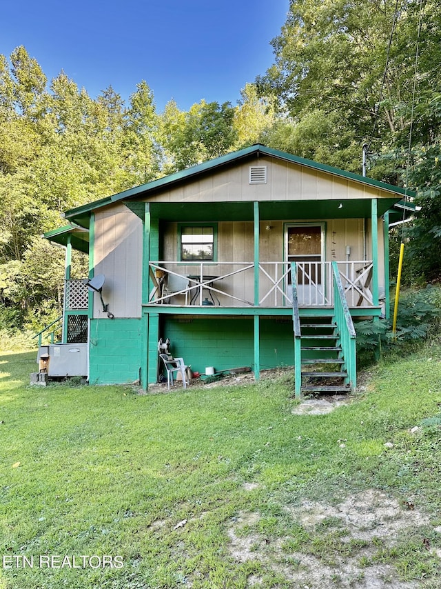 rear view of house featuring concrete block siding, a porch, and a yard