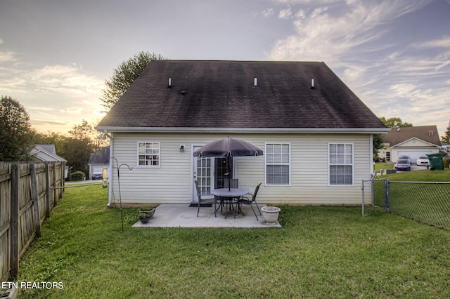 back house at dusk featuring a patio and a lawn