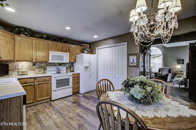 kitchen with white appliances, hardwood / wood-style flooring, an inviting chandelier, tasteful backsplash, and decorative light fixtures