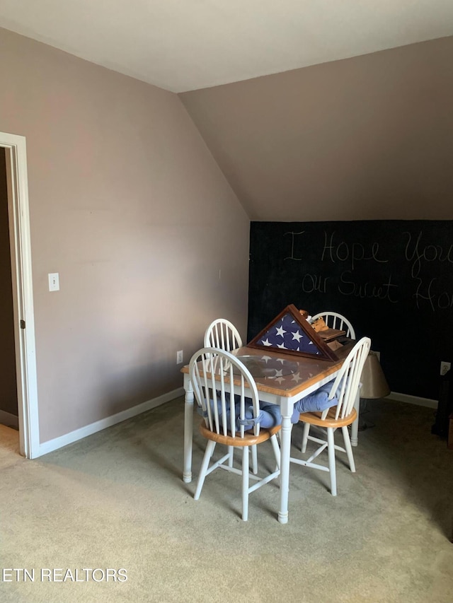 carpeted dining space with lofted ceiling and baseboards