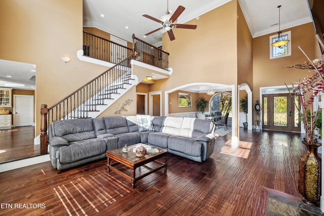 living room featuring a towering ceiling, ornamental molding, wood-type flooring, and ceiling fan