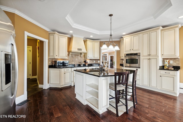 kitchen with pendant lighting, appliances with stainless steel finishes, cream cabinetry, and dark hardwood / wood-style floors