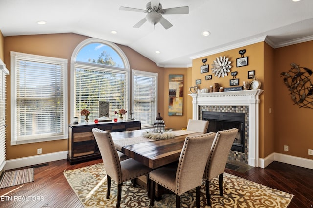 dining space with dark hardwood / wood-style flooring, a tile fireplace, ceiling fan, lofted ceiling, and crown molding