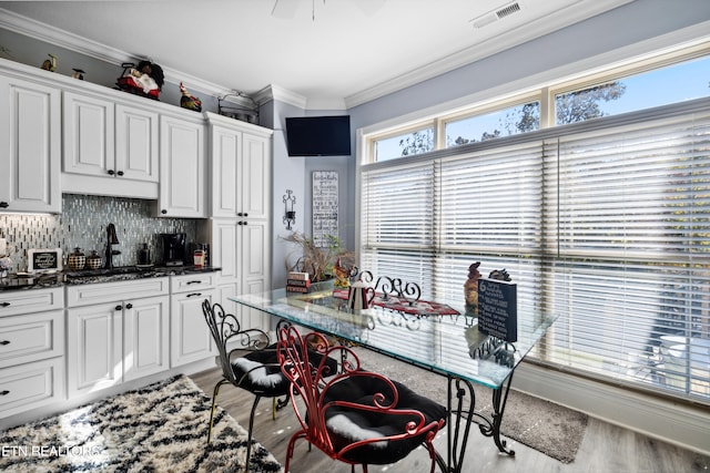 kitchen with backsplash, dark stone countertops, ornamental molding, light wood-type flooring, and white cabinets