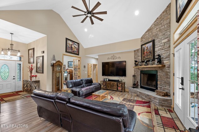 living room featuring ceiling fan, a stone fireplace, light hardwood / wood-style floors, and high vaulted ceiling