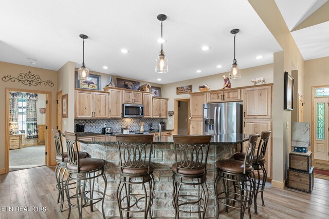 kitchen with a breakfast bar, stainless steel appliances, hanging light fixtures, and light wood-type flooring