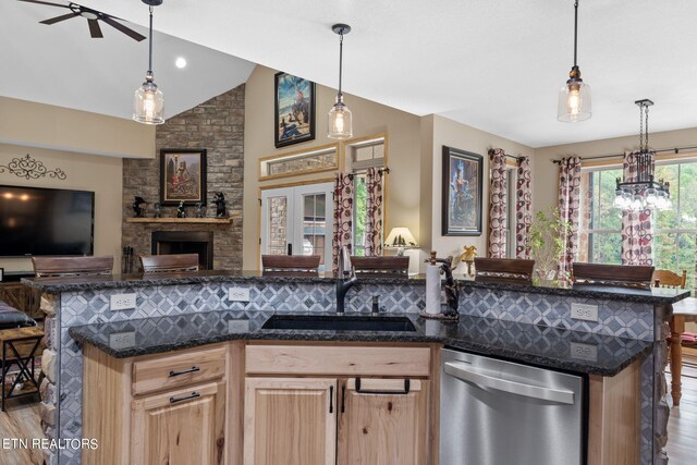 kitchen with dark stone countertops, ceiling fan with notable chandelier, a fireplace, dishwasher, and light hardwood / wood-style flooring