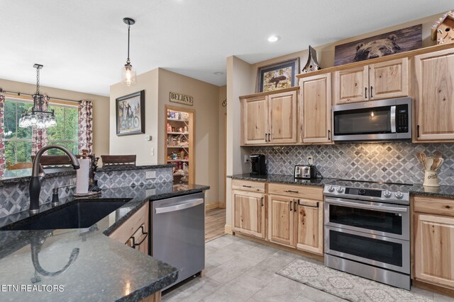 kitchen with pendant lighting, appliances with stainless steel finishes, dark stone counters, and sink