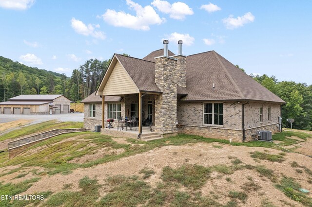 rear view of property with a garage, a patio, central AC, a yard, and an outbuilding