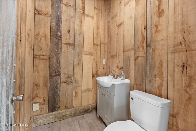 bathroom featuring wooden walls, hardwood / wood-style flooring, vanity, and toilet