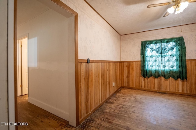 unfurnished room featuring a textured ceiling, ceiling fan, wooden walls, and dark hardwood / wood-style floors