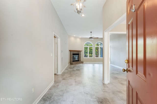 foyer entrance with ceiling fan with notable chandelier and a brick fireplace