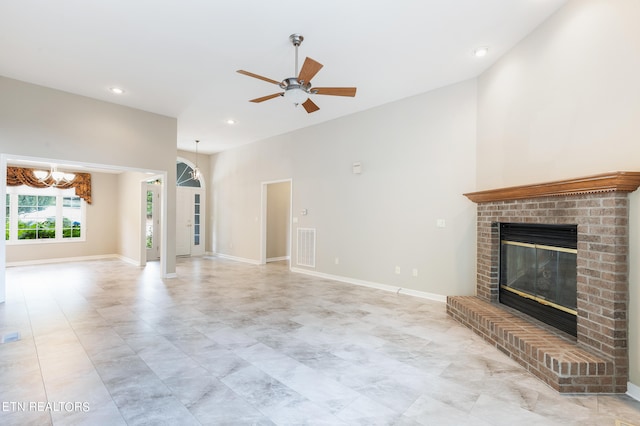 unfurnished living room featuring a brick fireplace, ceiling fan with notable chandelier, and a towering ceiling