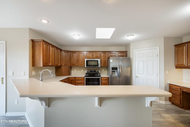 kitchen with a kitchen breakfast bar, light wood-type flooring, kitchen peninsula, and appliances with stainless steel finishes