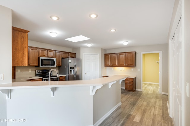 kitchen with a skylight, kitchen peninsula, appliances with stainless steel finishes, a breakfast bar area, and light hardwood / wood-style floors