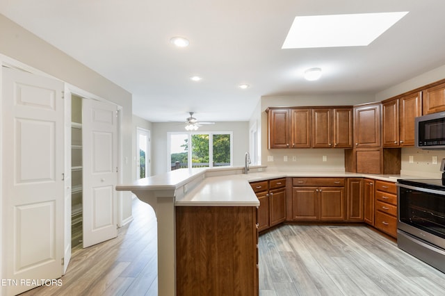 kitchen featuring light hardwood / wood-style floors, kitchen peninsula, a skylight, appliances with stainless steel finishes, and ceiling fan