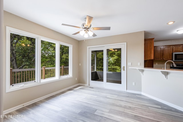 interior space with ceiling fan, kitchen peninsula, stainless steel appliances, light wood-type flooring, and a kitchen bar