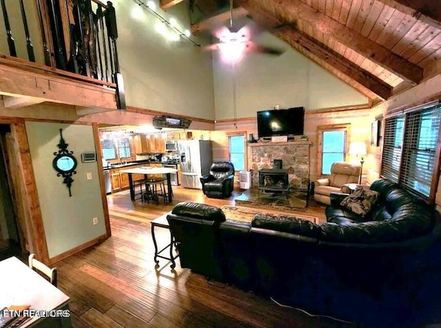 living room featuring high vaulted ceiling, a fireplace, beam ceiling, ceiling fan, and hardwood / wood-style flooring