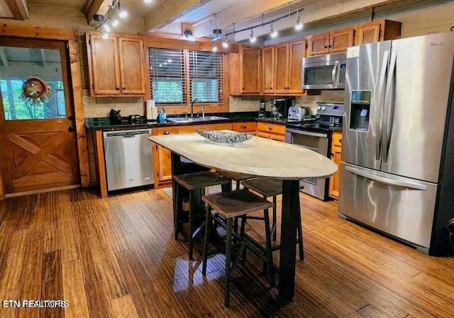 kitchen featuring beamed ceiling, stainless steel appliances, sink, and light hardwood / wood-style flooring