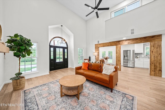 living room featuring light wood-type flooring, ceiling fan with notable chandelier, and high vaulted ceiling