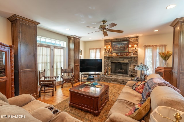 living room with ornate columns, ceiling fan, a stone fireplace, and light hardwood / wood-style flooring