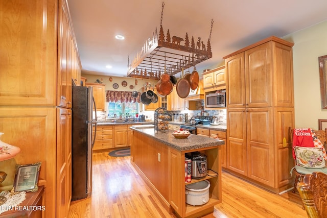 kitchen with light hardwood / wood-style floors, sink, decorative backsplash, an island with sink, and appliances with stainless steel finishes