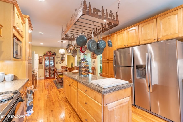 kitchen featuring stainless steel appliances, light hardwood / wood-style floors, a center island, and dark stone countertops