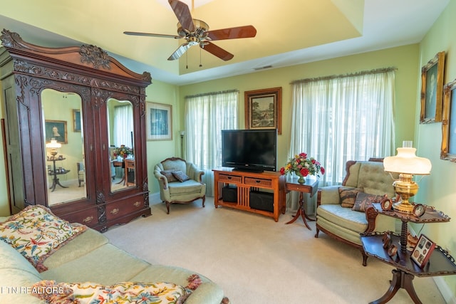 living room featuring ceiling fan, light colored carpet, a tray ceiling, and plenty of natural light