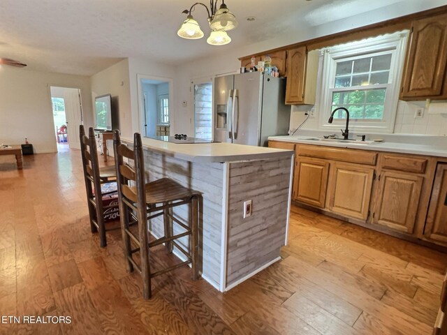 kitchen featuring hanging light fixtures, light hardwood / wood-style flooring, a chandelier, sink, and stainless steel refrigerator with ice dispenser