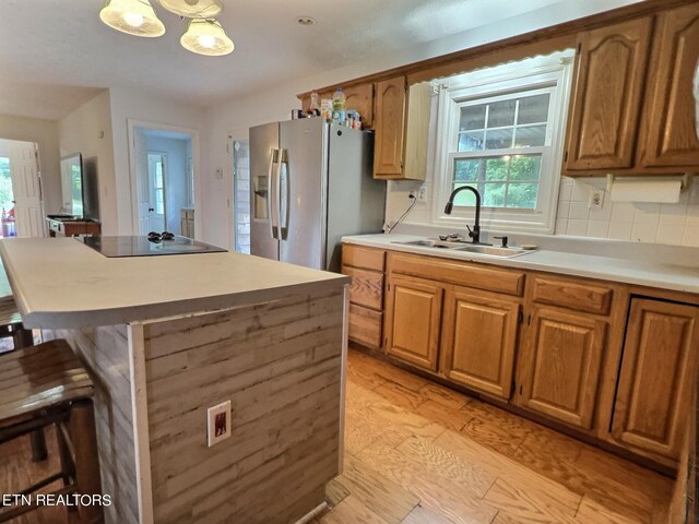 kitchen with stainless steel refrigerator with ice dispenser, pendant lighting, light hardwood / wood-style flooring, sink, and black electric stovetop