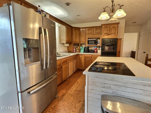 kitchen featuring an inviting chandelier, decorative light fixtures, black appliances, sink, and light wood-type flooring