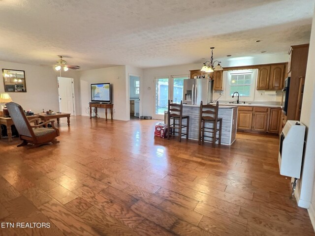 dining area with heating unit, ceiling fan with notable chandelier, sink, wood-type flooring, and a textured ceiling