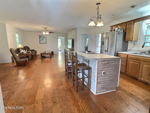 kitchen featuring ceiling fan with notable chandelier, a center island, sink, stainless steel fridge with ice dispenser, and light hardwood / wood-style floors