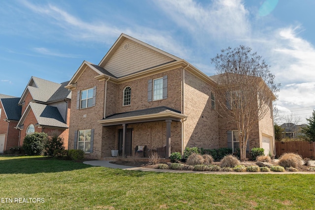 traditional-style house featuring an attached garage, covered porch, fence, a front yard, and brick siding