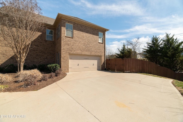 view of side of property featuring a garage, driveway, fence, and brick siding