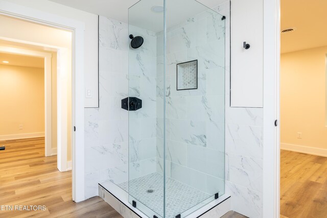 bathroom with tiled shower and hardwood / wood-style floors