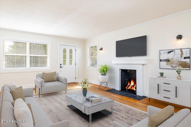 living room featuring light wood-type flooring, crown molding, plenty of natural light, and a brick fireplace