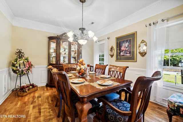 dining area featuring light wood-type flooring, ornamental molding, and a notable chandelier