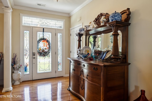 foyer entrance with light wood-type flooring, crown molding, and ornate columns