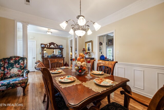 dining space featuring light wood-type flooring, crown molding, decorative columns, and a chandelier