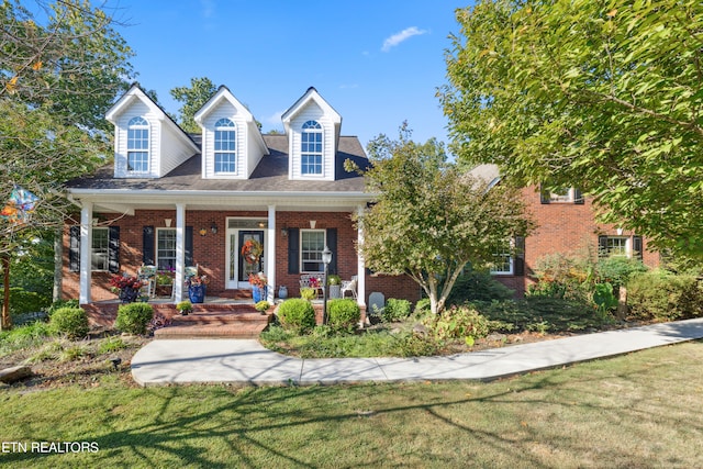 cape cod-style house featuring a front yard and covered porch