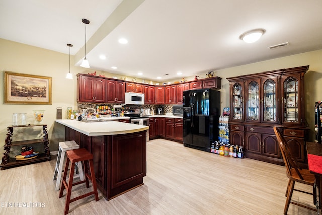 kitchen with tasteful backsplash, kitchen peninsula, a breakfast bar area, stainless steel appliances, and light hardwood / wood-style flooring