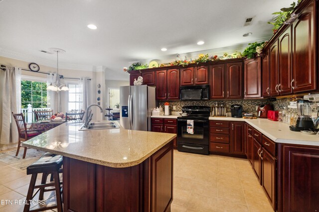 kitchen with sink, a center island with sink, decorative light fixtures, a chandelier, and black appliances