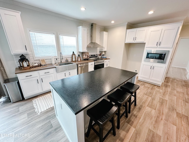 kitchen featuring appliances with stainless steel finishes, white cabinetry, sink, decorative backsplash, and wall chimney range hood